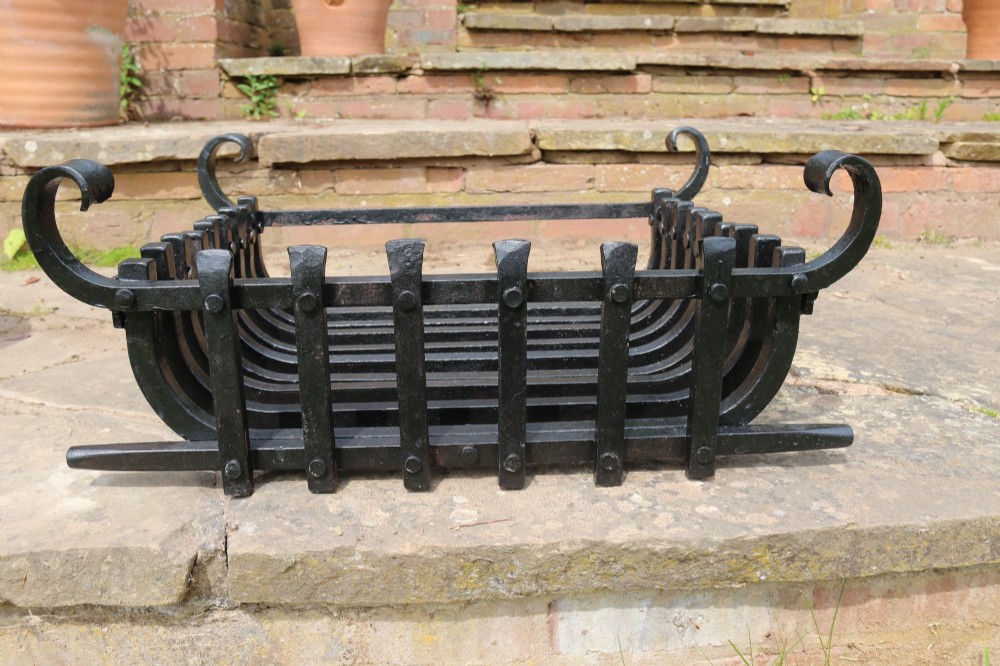 A black wrought iron fire basket featuring vertical slatted bars, hand-riveted joints, and scrolled corner handles.