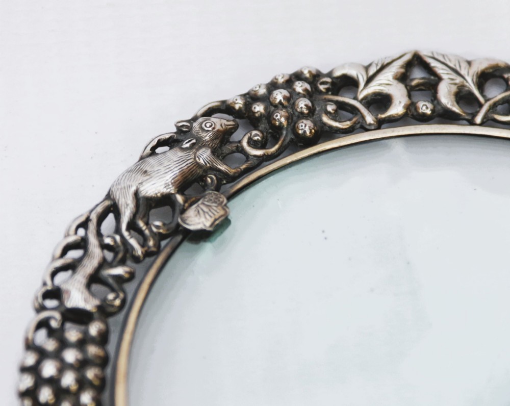 An antique Chinese magnifying glass featuring an ornate repousse silver circular frame decorated with squirrels and grapevines attached to a carved off-white jade handle. View III