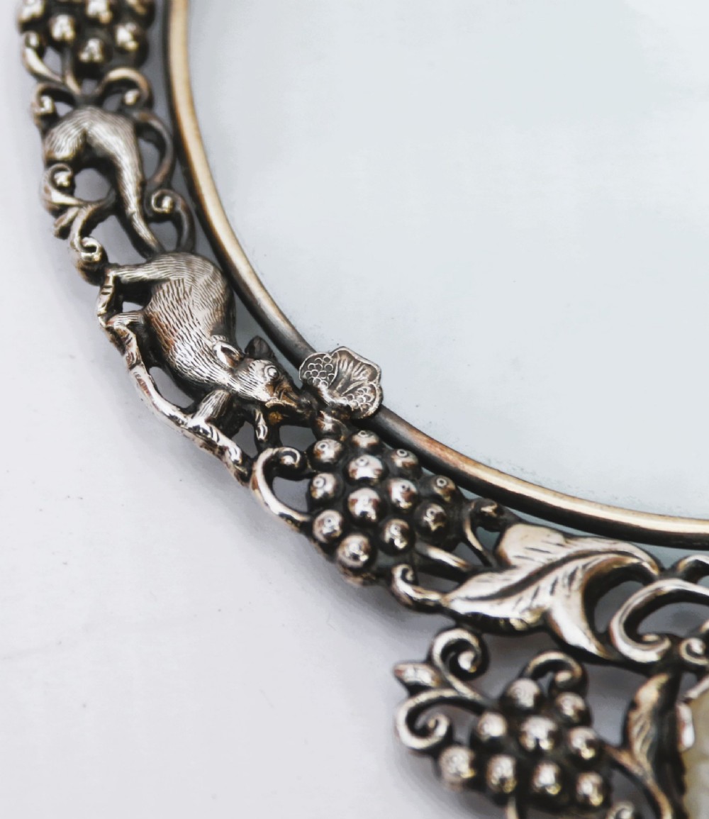 An antique Chinese magnifying glass featuring an ornate repousse silver circular frame decorated with squirrels and grapevines attached to a carved off-white jade handle. View VII