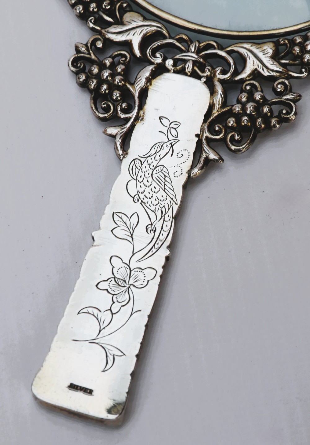 An antique Chinese magnifying glass featuring an ornate repousse silver circular frame decorated with squirrels and grapevines attached to a carved off-white jade handle. View IX