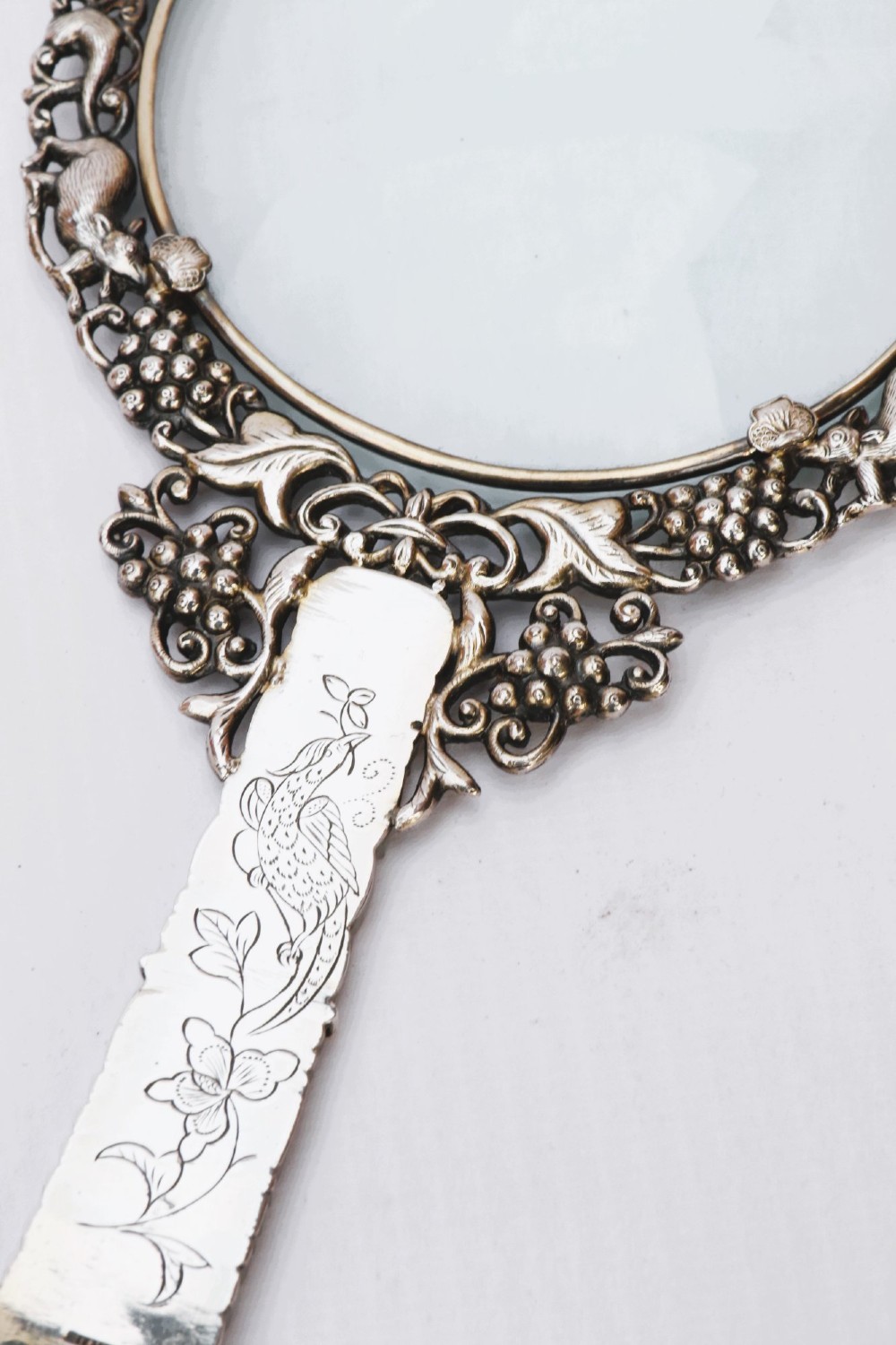 An antique Chinese magnifying glass featuring an ornate repousse silver circular frame decorated with squirrels and grapevines attached to a carved off-white jade handle. View XI