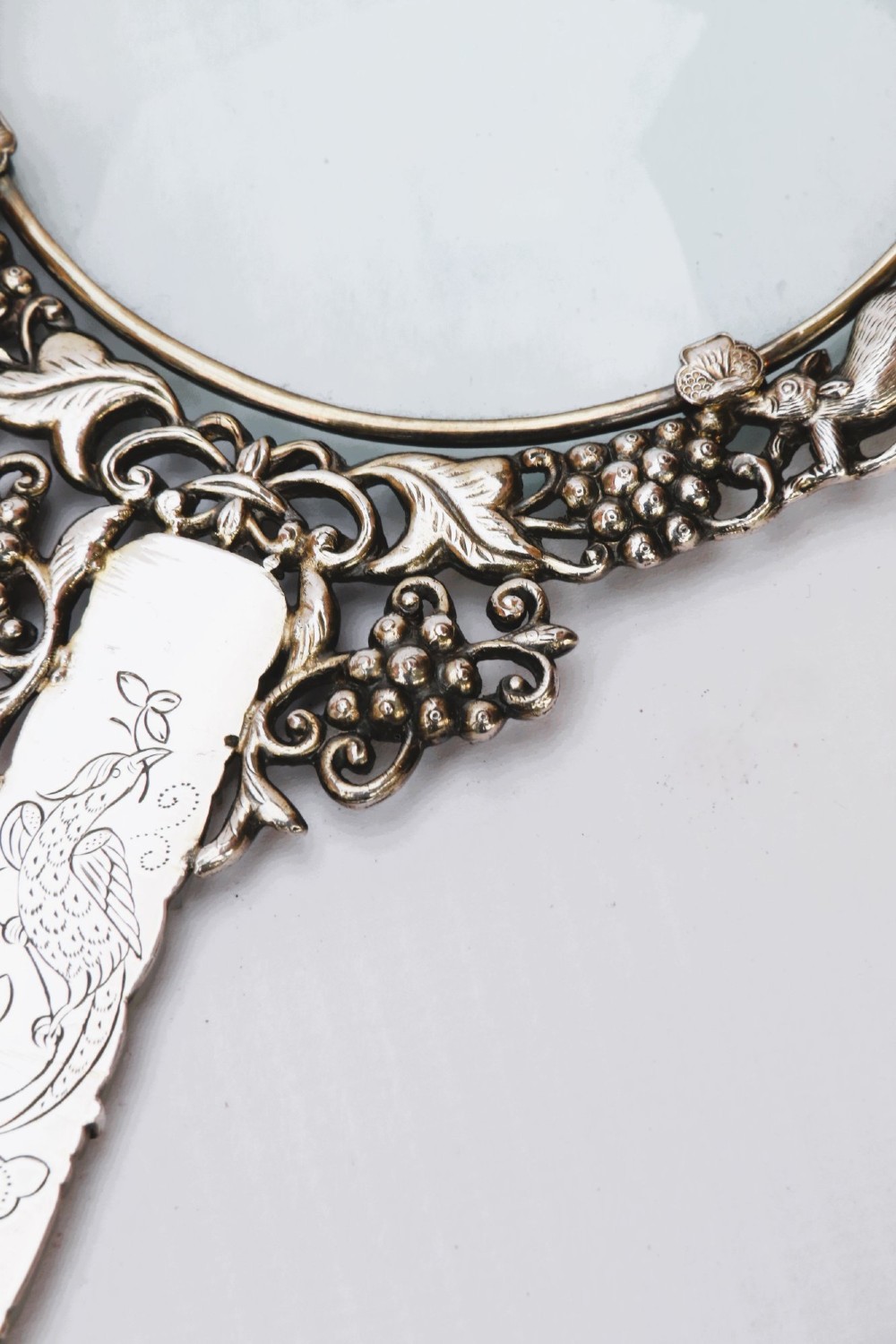 An antique Chinese magnifying glass featuring an ornate repousse silver circular frame decorated with squirrels and grapevines attached to a carved off-white jade handle. View XII