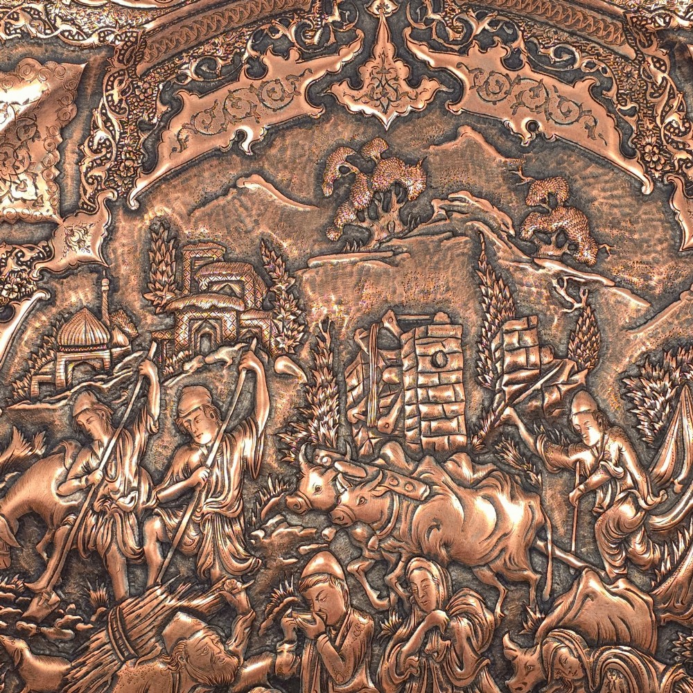 A circular 19th-century Persian copper charger plate featuring dense repousse and engraved figural and landscape scenes surrounded by ornate floral borders. View V