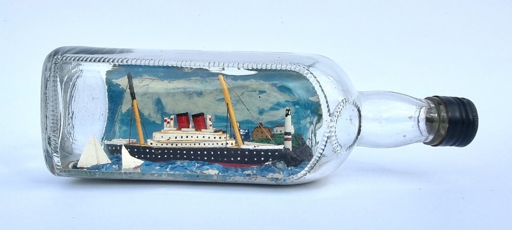 A horizontal glass bottle containing a handcrafted 1930s steamship diorama with red funnels, a painted blue sea, and a lighthouse background.
