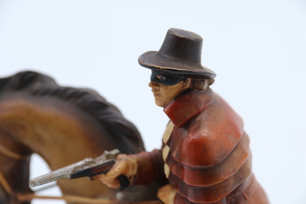 An Art Deco cold-painted metal table lighter depicting a masked figure on horseback mounted on a wooden base. View X