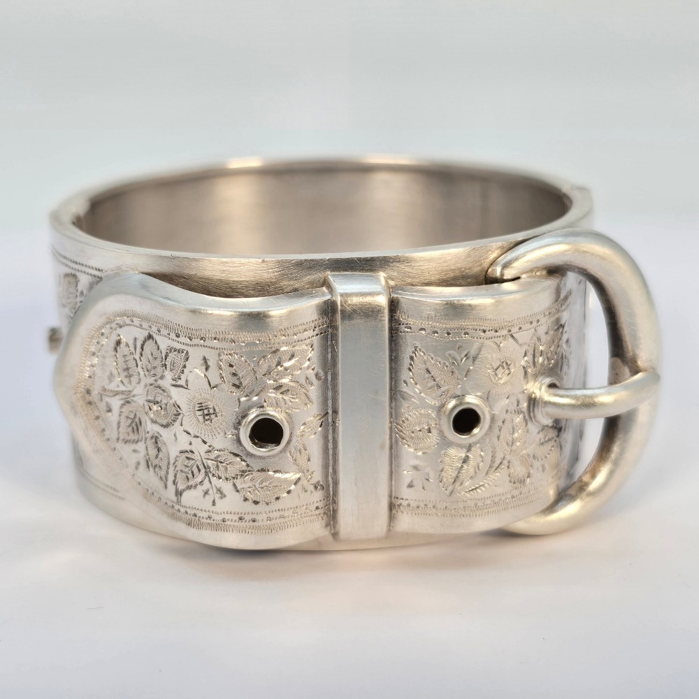A wide Victorian sterling silver hinged bangle crafted with a functional buckle motif and detailed hand-engraved foliage patterns. View II