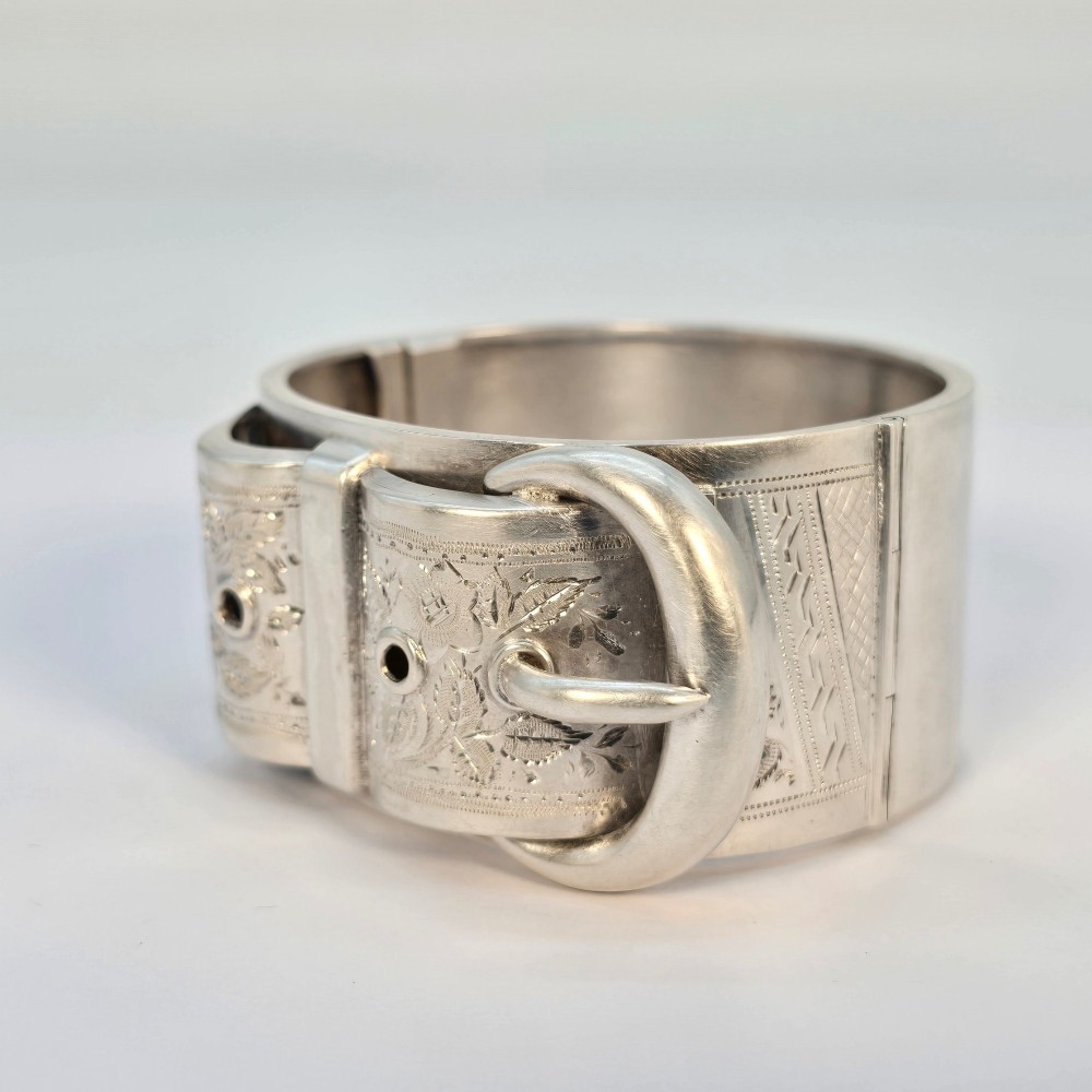 A wide Victorian sterling silver hinged bangle crafted with a functional buckle motif and detailed hand-engraved foliage patterns. View III