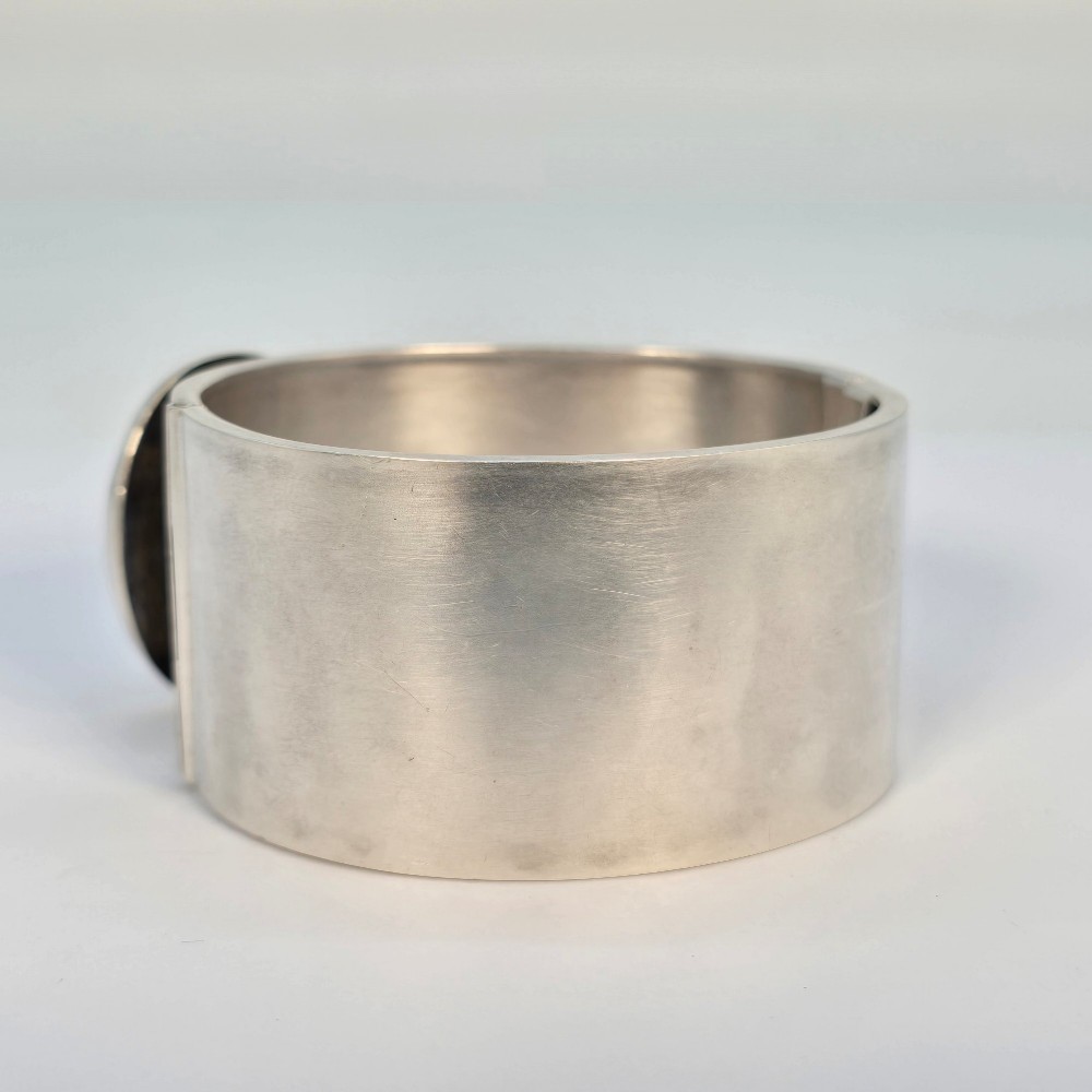 A wide Victorian sterling silver hinged bangle crafted with a functional buckle motif and detailed hand-engraved foliage patterns. View IV