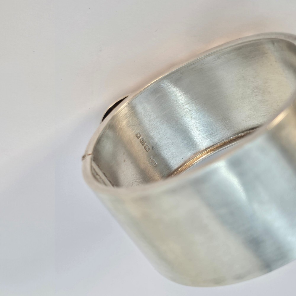 A wide Victorian sterling silver hinged bangle crafted with a functional buckle motif and detailed hand-engraved foliage patterns. View V