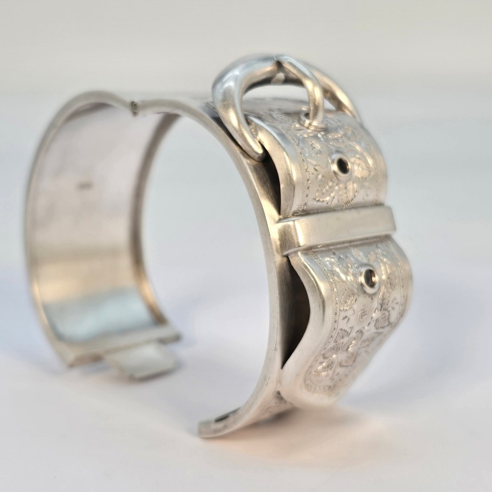 A wide Victorian sterling silver hinged bangle crafted with a functional buckle motif and detailed hand-engraved foliage patterns. View VIII