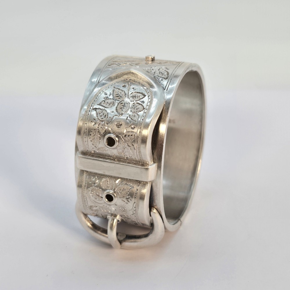 A wide Victorian sterling silver hinged bangle crafted with a functional buckle motif and detailed hand-engraved foliage patterns. View XI