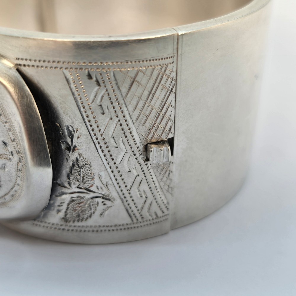 A wide Victorian sterling silver hinged bangle crafted with a functional buckle motif and detailed hand-engraved foliage patterns. View XII