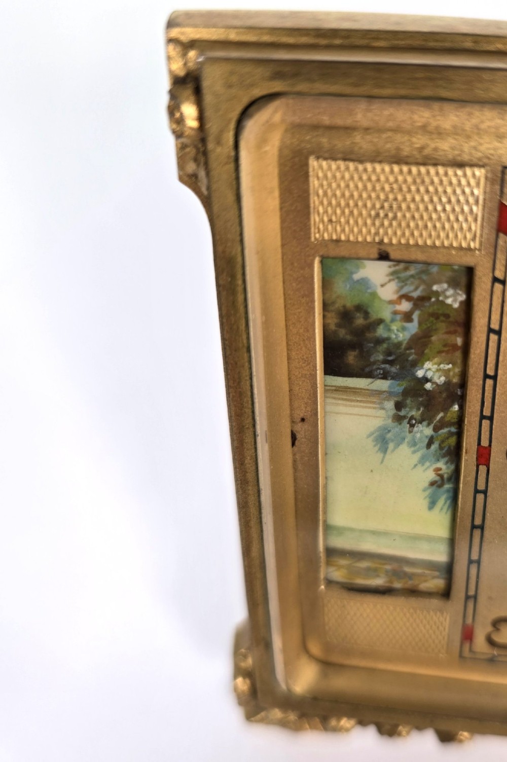 A rectangular gilt brass Art Deco strut clock featuring an illustrated courtly scene on the central dial surrounded by numeric markers. View VII