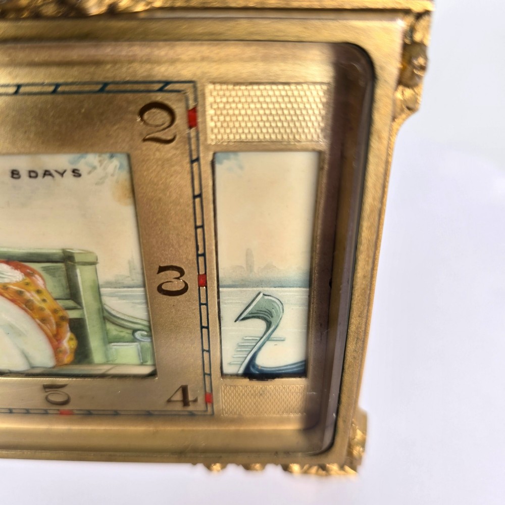 A rectangular gilt brass Art Deco strut clock featuring an illustrated courtly scene on the central dial surrounded by numeric markers. View VIII