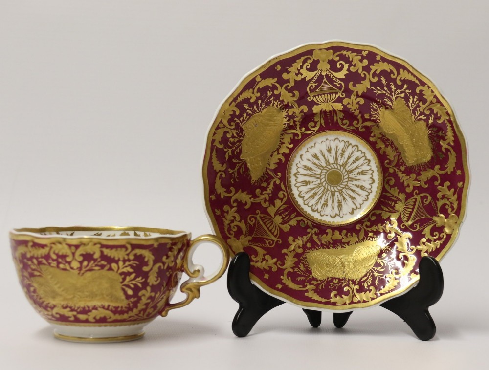 An early nineteenth-century Regency Spode porcelain cabinet cup and saucer featuring deep crimson ground decorated with heavy gilded scrollwork and shell motifs.