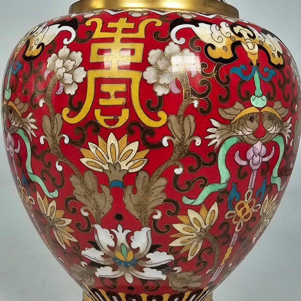 A matching pair of baluster-form Chinese cloisonne enamel vases with red backgrounds, lotus motifs, auspicious symbols, and gilt rims. View XII
