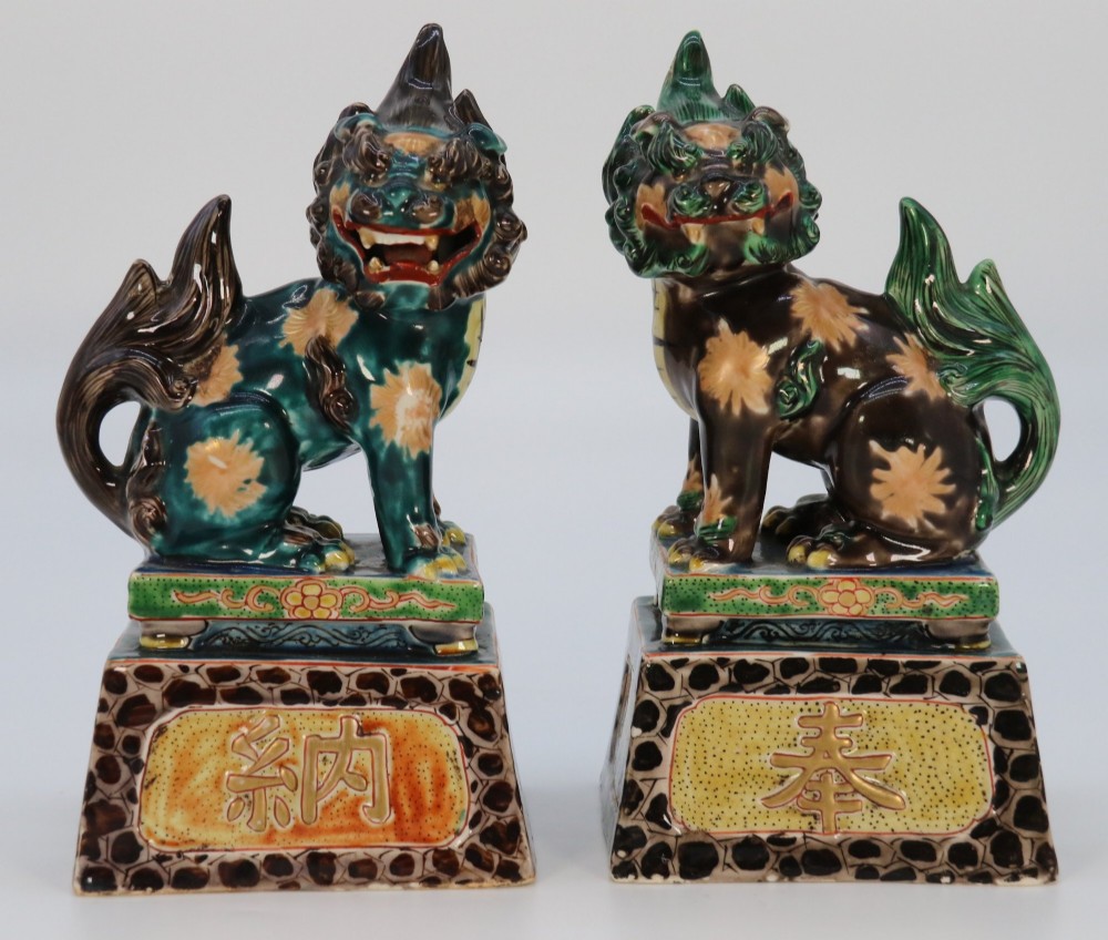 A pair of glazed Chinese ceramic Buddhist lion figures decorated in green, brown, and yellow glazes resting on patterned pedestal bases.
