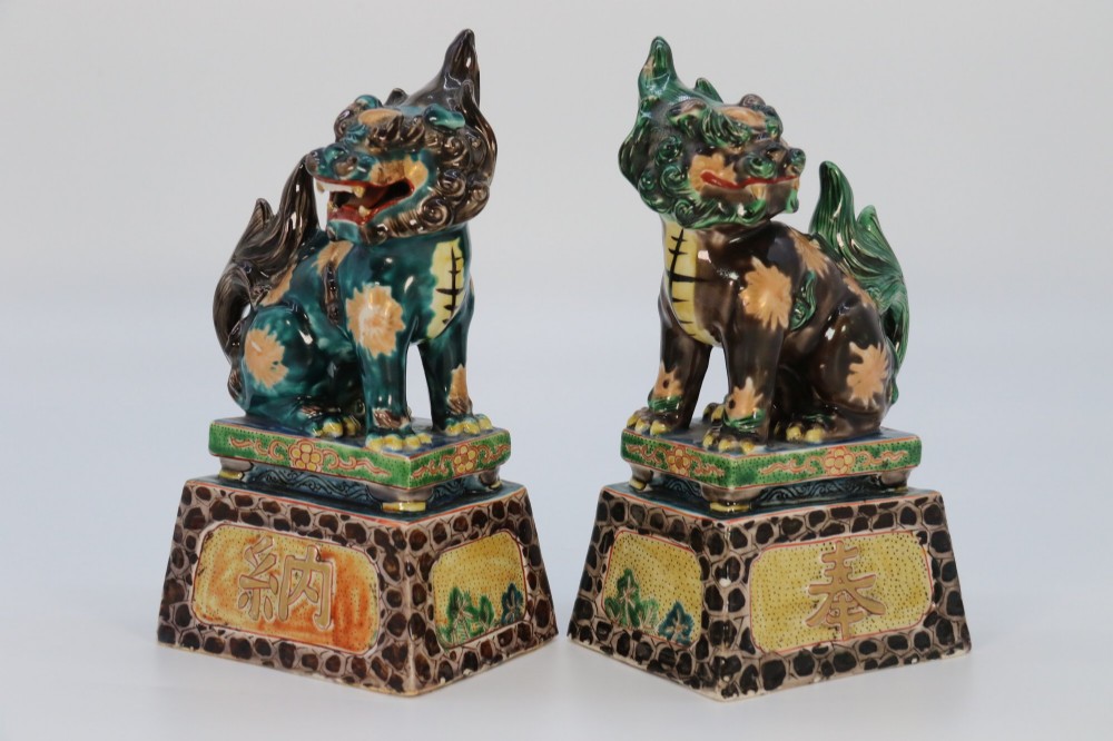 A pair of glazed Chinese ceramic Buddhist lion figures decorated in green, brown, and yellow glazes resting on patterned pedestal bases. View II