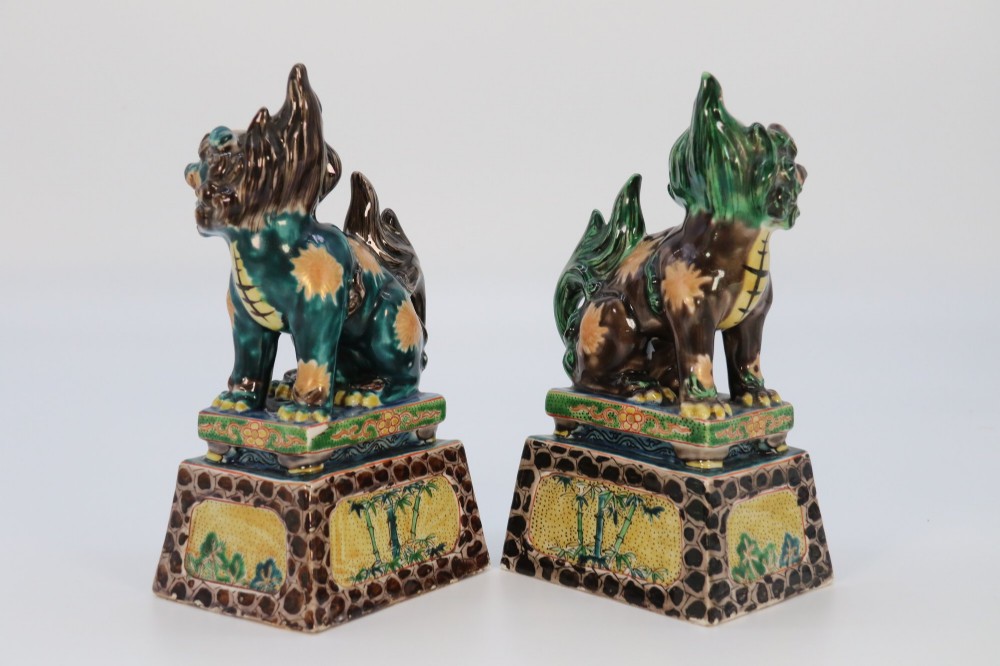 A pair of glazed Chinese ceramic Buddhist lion figures decorated in green, brown, and yellow glazes resting on patterned pedestal bases. View V