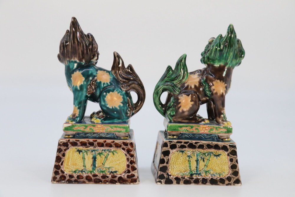A pair of glazed Chinese ceramic Buddhist lion figures decorated in green, brown, and yellow glazes resting on patterned pedestal bases. View VI