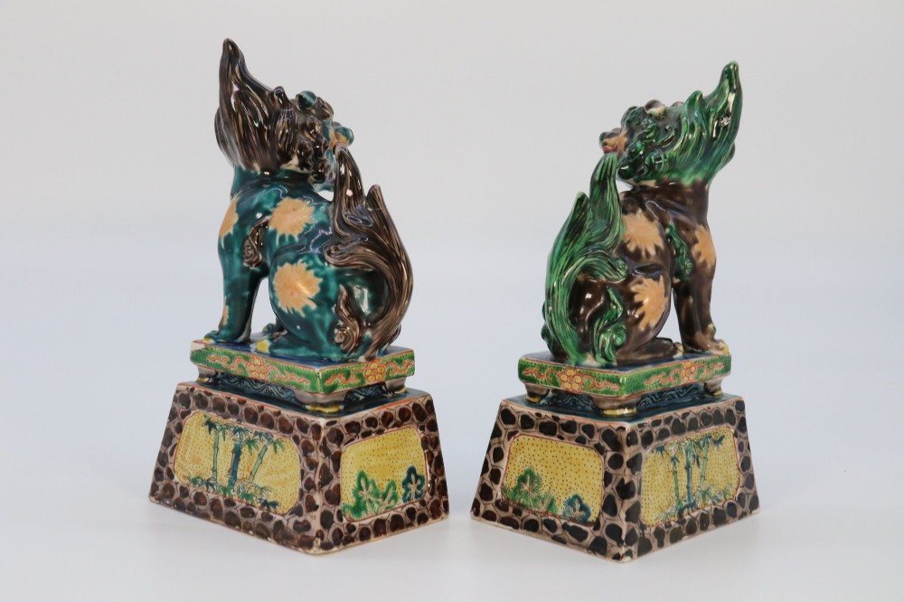 A pair of glazed Chinese ceramic Buddhist lion figures decorated in green, brown, and yellow glazes resting on patterned pedestal bases. View VII