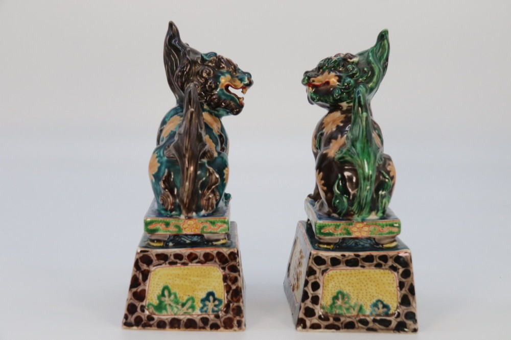 A pair of glazed Chinese ceramic Buddhist lion figures decorated in green, brown, and yellow glazes resting on patterned pedestal bases. View VIII