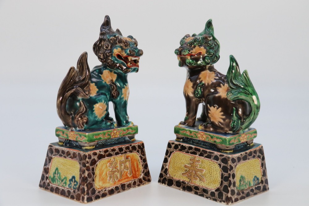 A pair of glazed Chinese ceramic Buddhist lion figures decorated in green, brown, and yellow glazes resting on patterned pedestal bases. View IX
