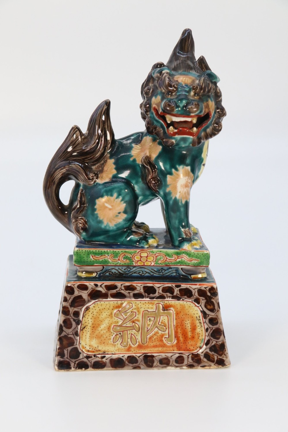 A pair of glazed Chinese ceramic Buddhist lion figures decorated in green, brown, and yellow glazes resting on patterned pedestal bases. View X