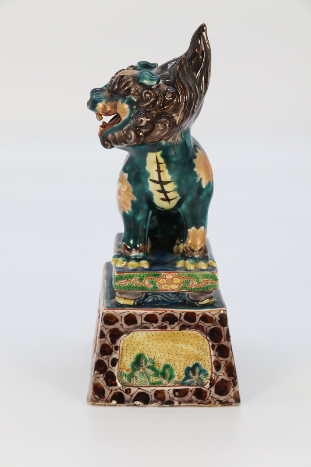A pair of glazed Chinese ceramic Buddhist lion figures decorated in green, brown, and yellow glazes resting on patterned pedestal bases. View XII