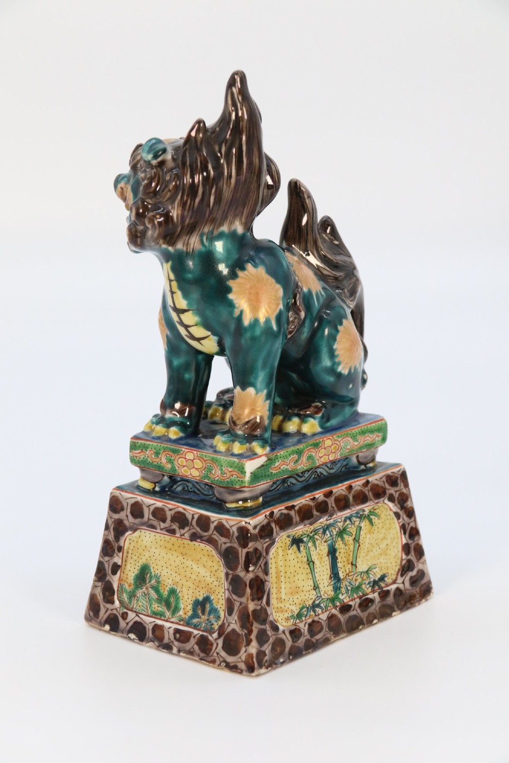 A pair of glazed Chinese ceramic Buddhist lion figures decorated in green, brown, and yellow glazes resting on patterned pedestal bases. View XIII