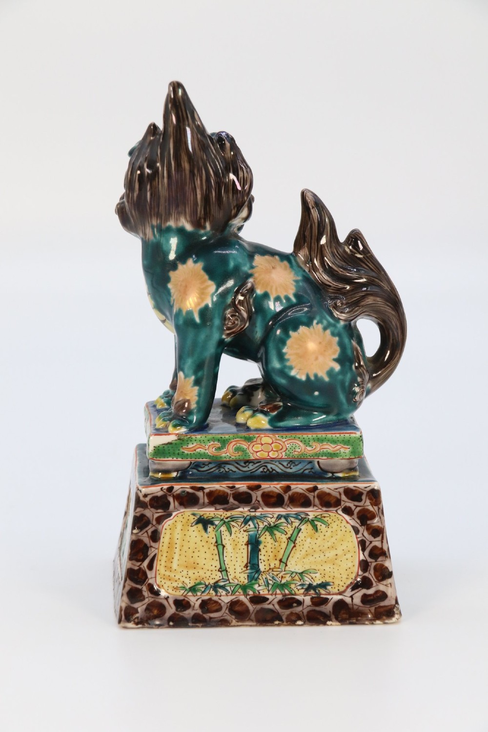 A pair of glazed Chinese ceramic Buddhist lion figures decorated in green, brown, and yellow glazes resting on patterned pedestal bases. View XIV