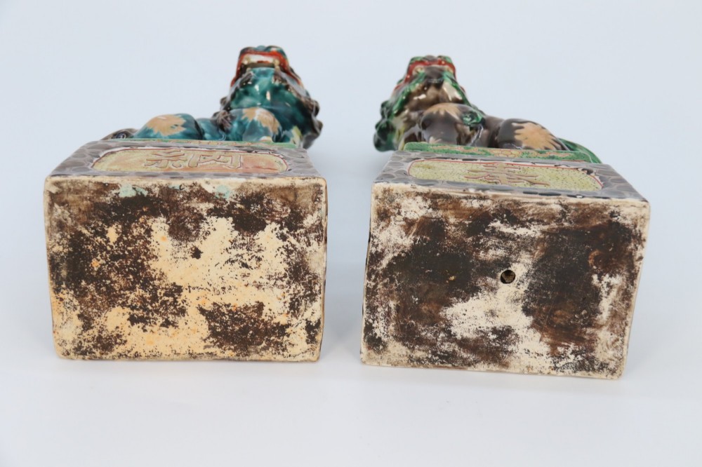 A pair of glazed Chinese ceramic Buddhist lion figures decorated in green, brown, and yellow glazes resting on patterned pedestal bases. View XV
