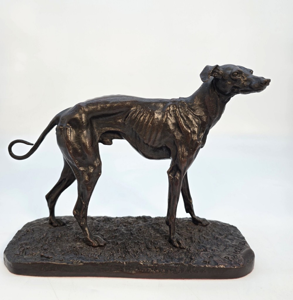 A 19th-century dark patinated bronze sculpture of a standing greyhound dog on a textured oval base. View II