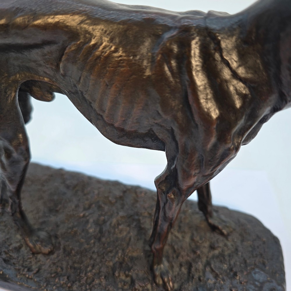 A 19th-century dark patinated bronze sculpture of a standing greyhound dog on a textured oval base. View IX