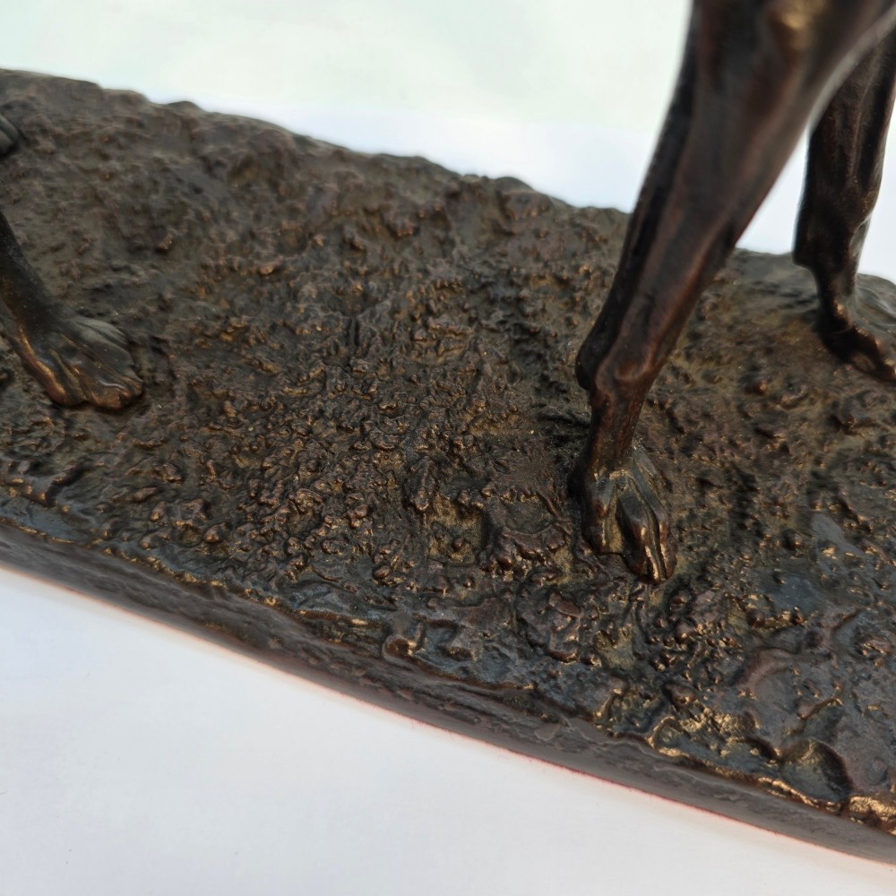 A 19th-century dark patinated bronze sculpture of a standing greyhound dog on a textured oval base. View X