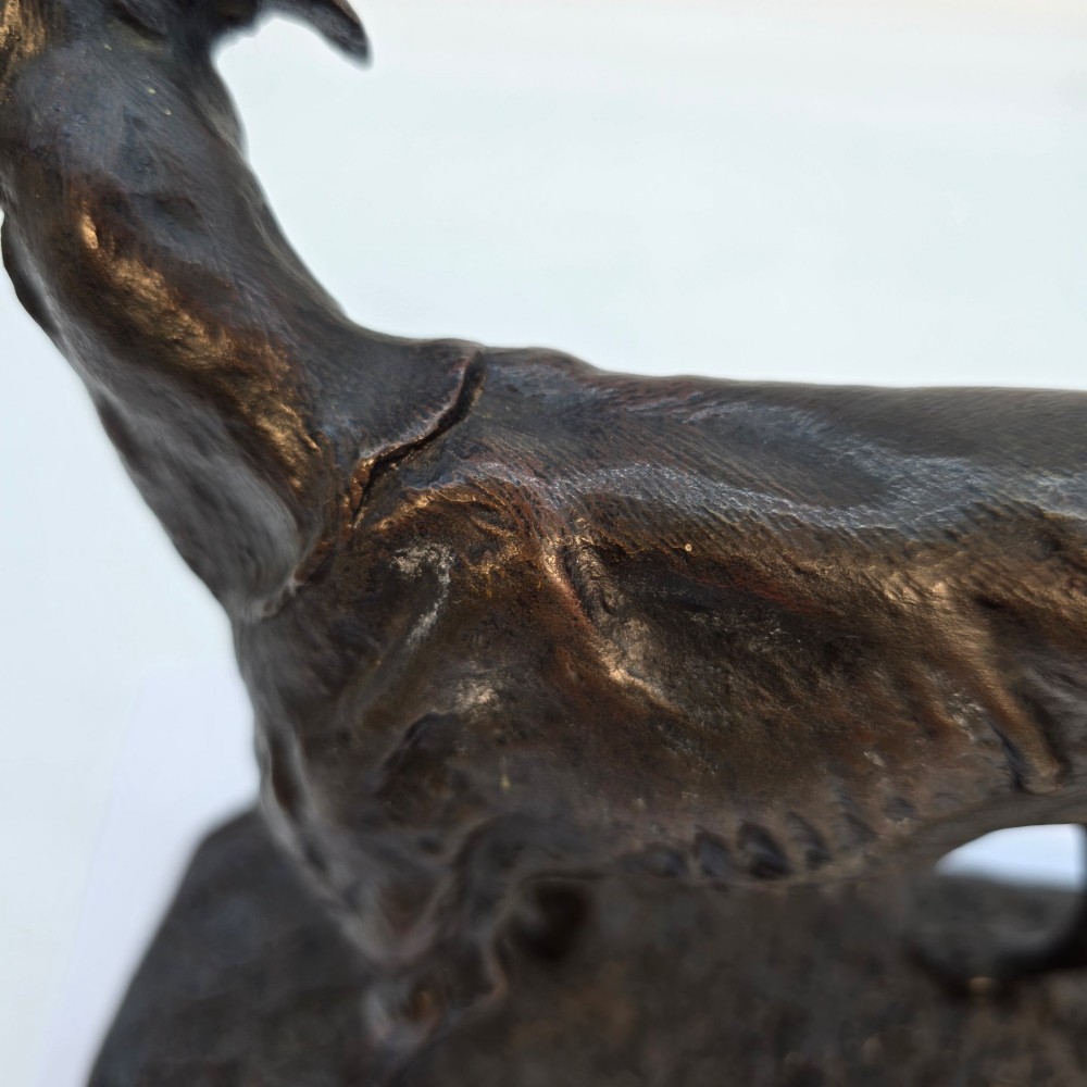 A 19th-century dark patinated bronze sculpture of a standing greyhound dog on a textured oval base. View XI