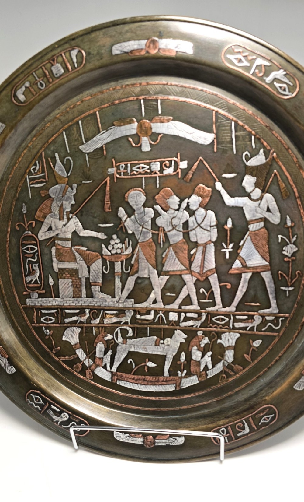 A circular bronze charger decorated with silver and copper inlays depicting pharaonic figures, hieroglyphs, and a winged sun deity. View II