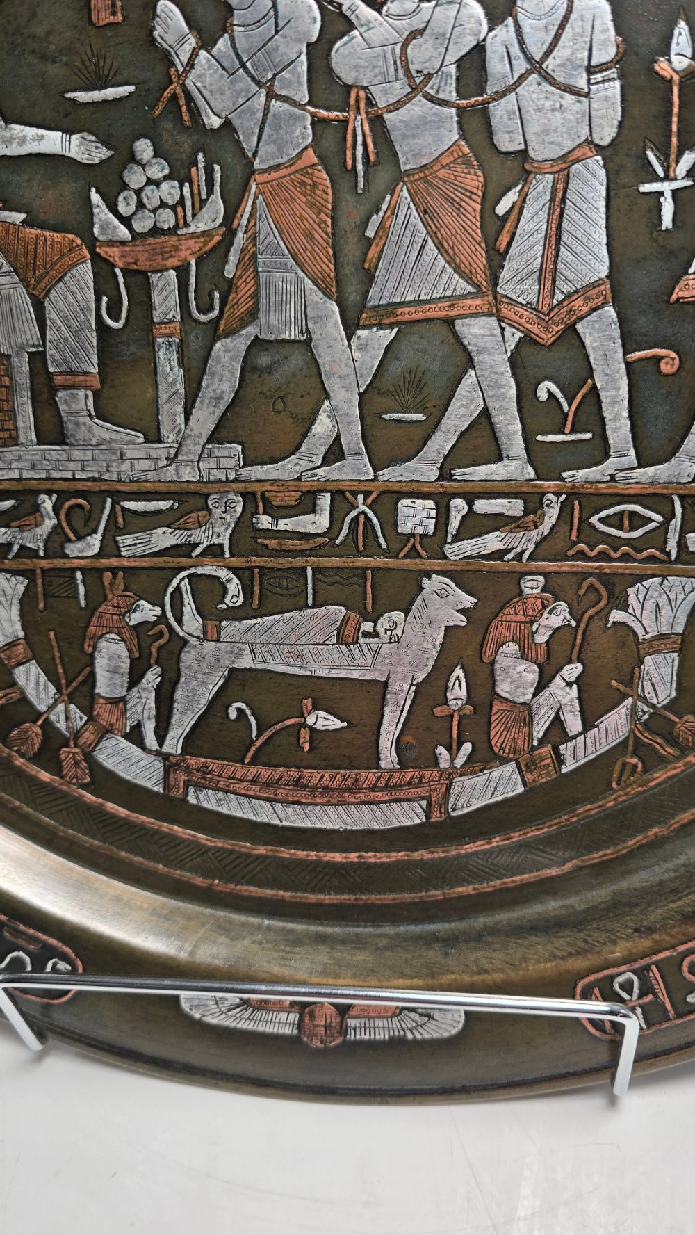 A circular bronze charger decorated with silver and copper inlays depicting pharaonic figures, hieroglyphs, and a winged sun deity. View V