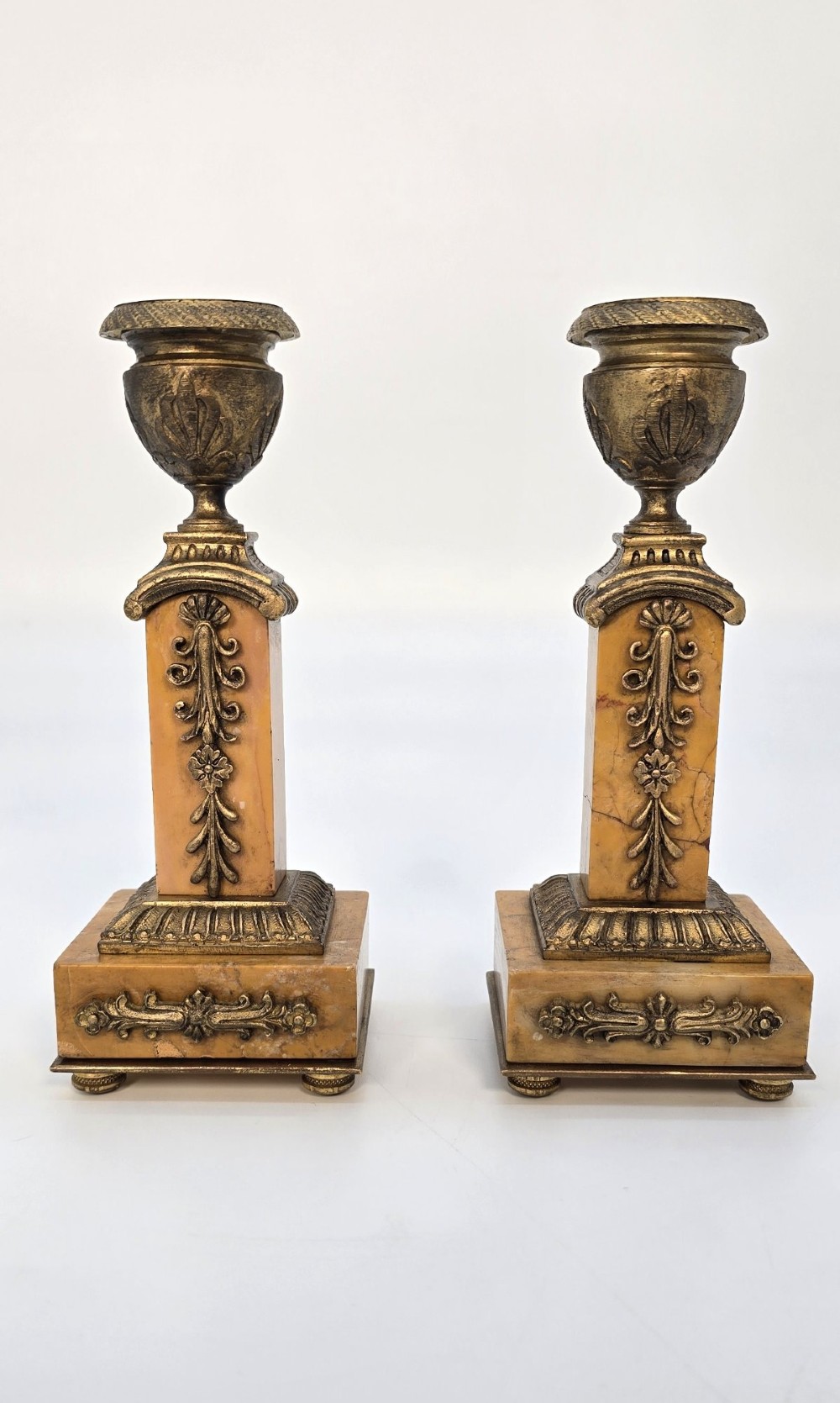 A pair of nineteenth-century French Empire gilt-bronze candlesticks featuring urn-shaped nozzles and applied bronze foliage on rectangular yellow marble bases.