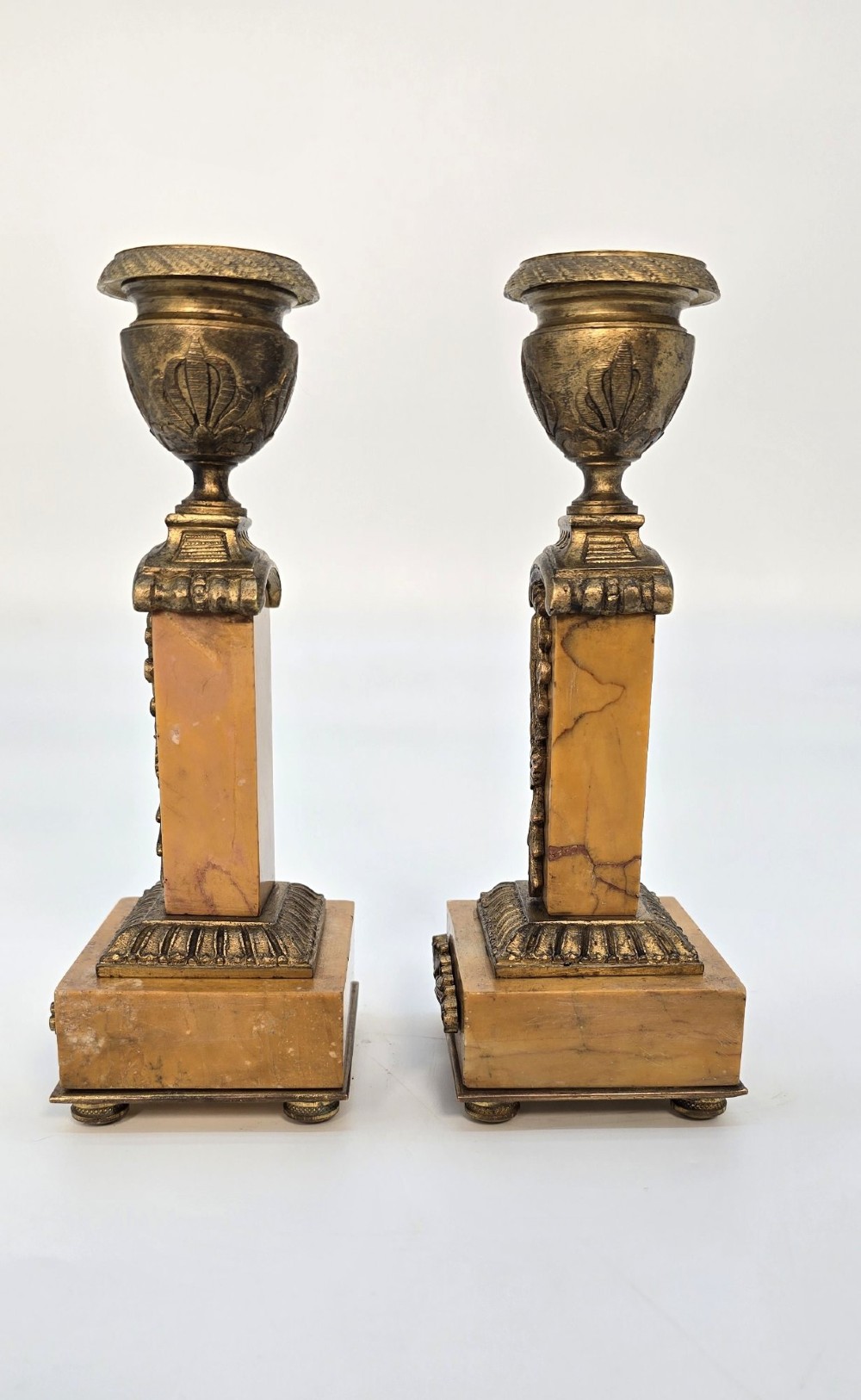A pair of nineteenth-century French Empire gilt-bronze candlesticks featuring urn-shaped nozzles and applied bronze foliage on rectangular yellow marble bases. View XII