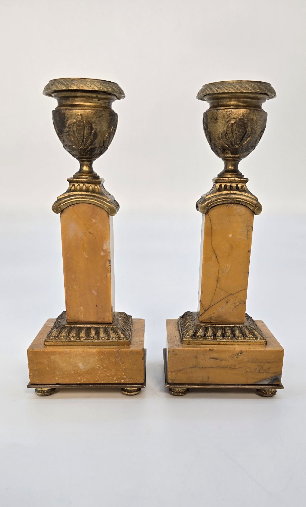 A pair of nineteenth-century French Empire gilt-bronze candlesticks featuring urn-shaped nozzles and applied bronze foliage on rectangular yellow marble bases. View XIV