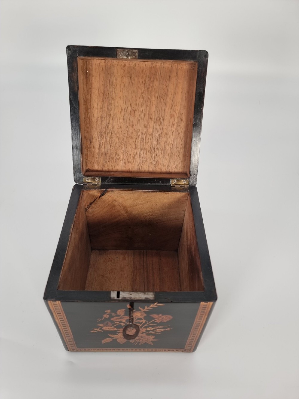 A square ebonised wooden box featuring detailed Sorrento marquetry inlay depicting figures on the top lid, floral motifs on the sides, and geometric borders. View IV