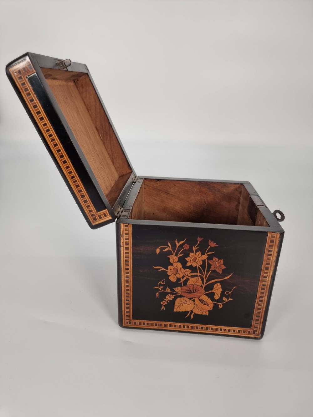 A square ebonised wooden box featuring detailed Sorrento marquetry inlay depicting figures on the top lid, floral motifs on the sides, and geometric borders. View IX