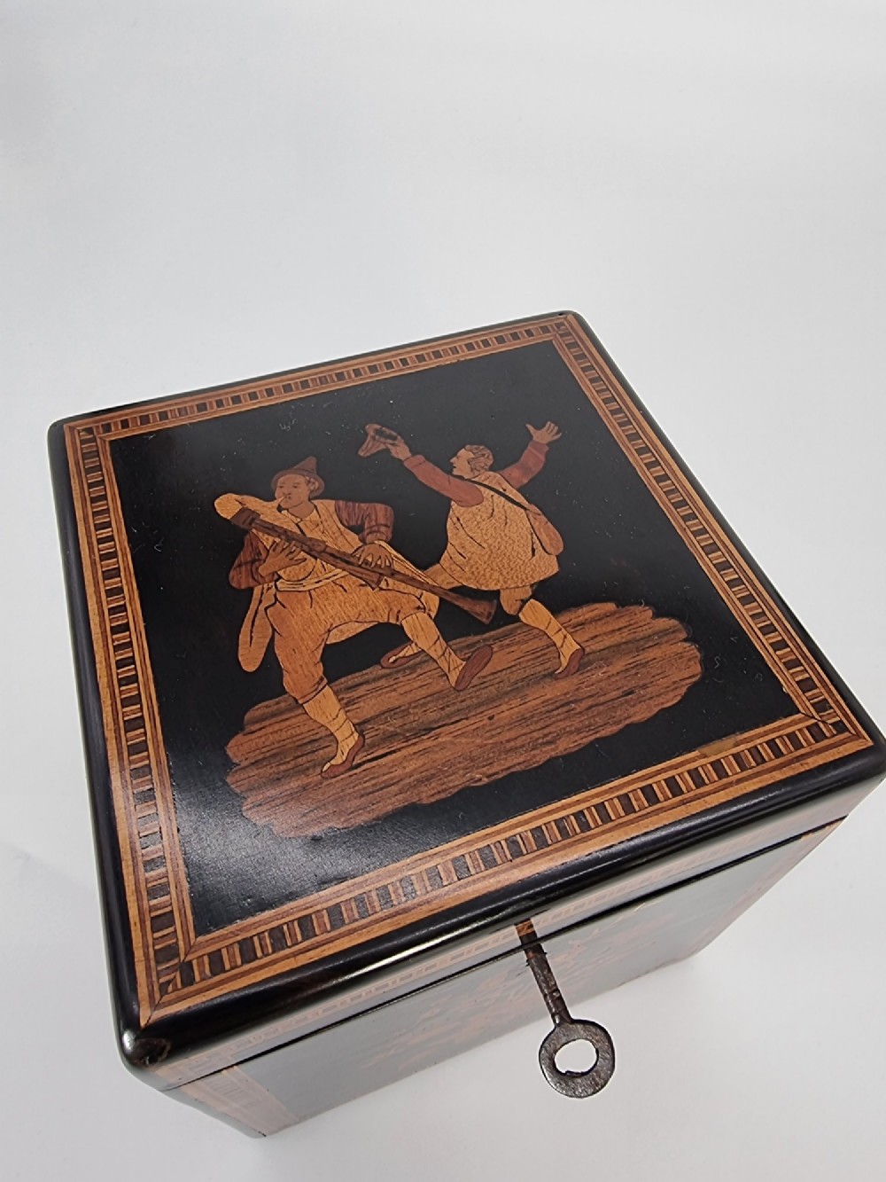 A square ebonised wooden box featuring detailed Sorrento marquetry inlay depicting figures on the top lid, floral motifs on the sides, and geometric borders. View XI