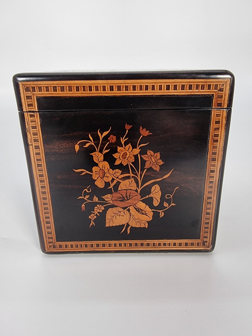 A square ebonised wooden box featuring detailed Sorrento marquetry inlay depicting figures on the top lid, floral motifs on the sides, and geometric borders. View XIII