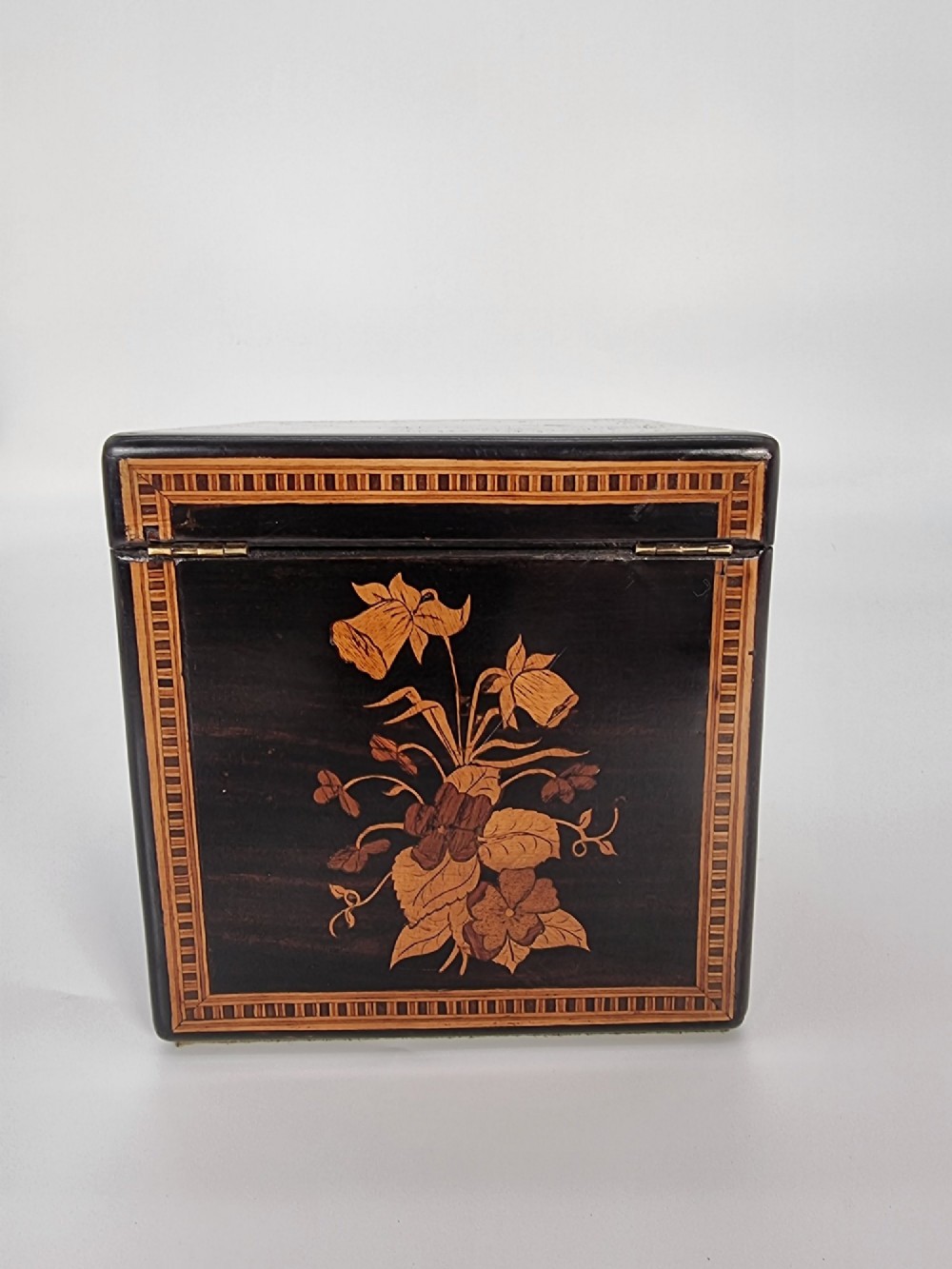 A square ebonised wooden box featuring detailed Sorrento marquetry inlay depicting figures on the top lid, floral motifs on the sides, and geometric borders. View XIV