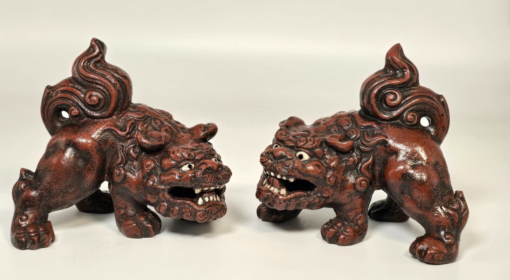 A pair of reddish-brown cast iron Chinoiserie guardian lions with swirling manes and open mouths displaying white painted teeth.