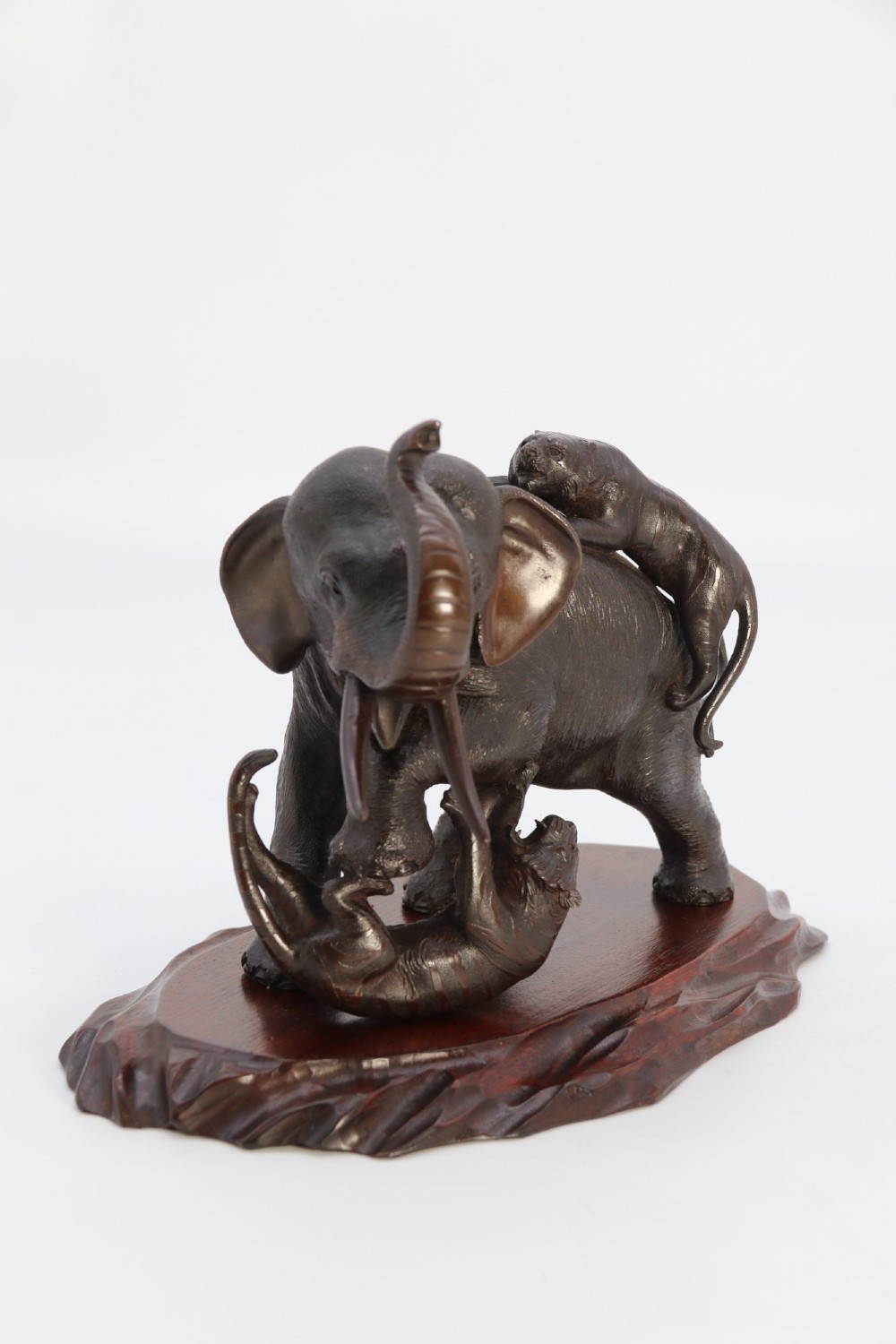 A dark patinated bronze sculpture of an elephant defending itself against two tigers, mounted on a carved wooden base. View III