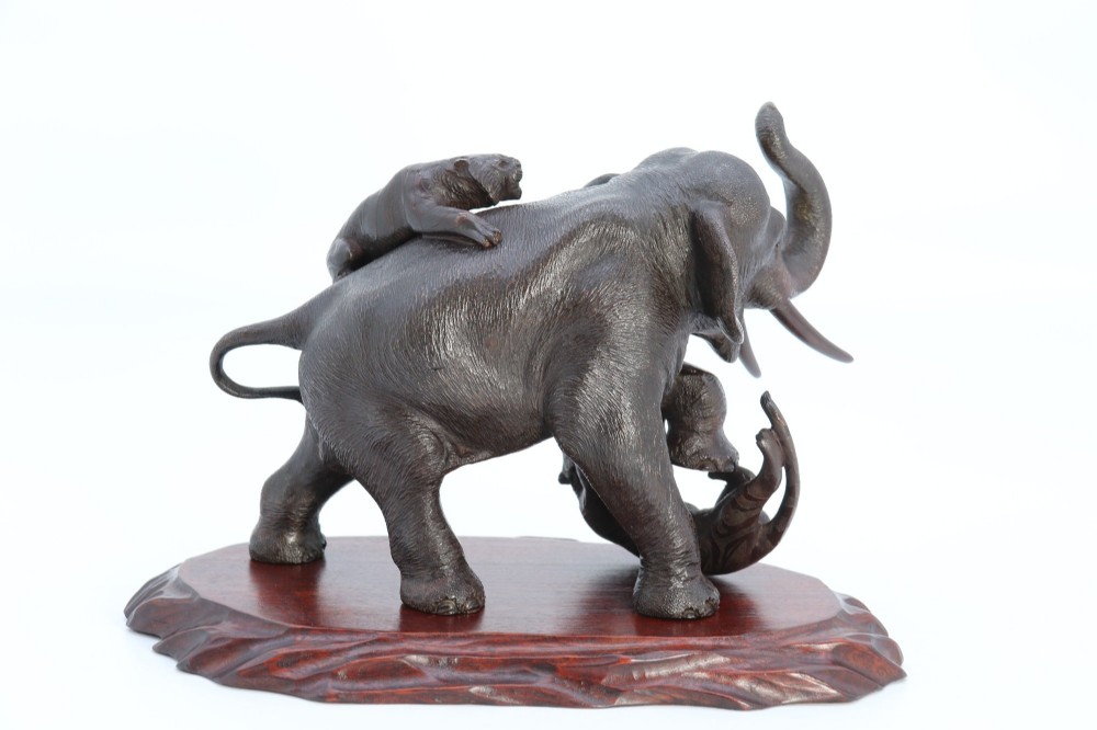 A dark patinated bronze sculpture of an elephant defending itself against two tigers, mounted on a carved wooden base. View VI