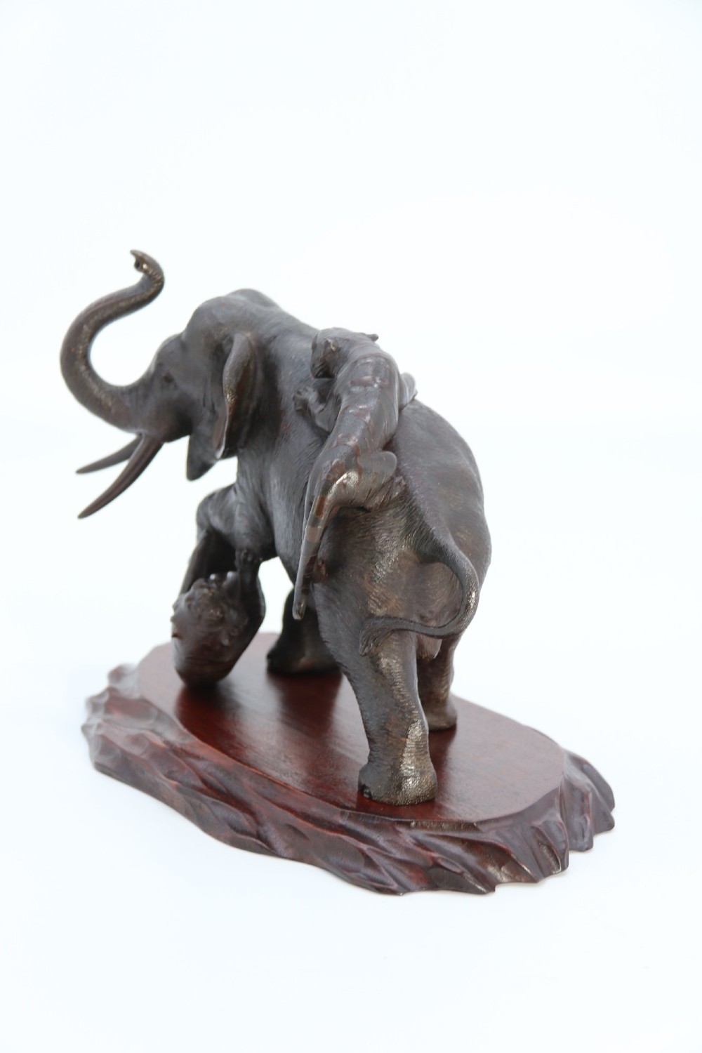 A dark patinated bronze sculpture of an elephant defending itself against two tigers, mounted on a carved wooden base. View IX